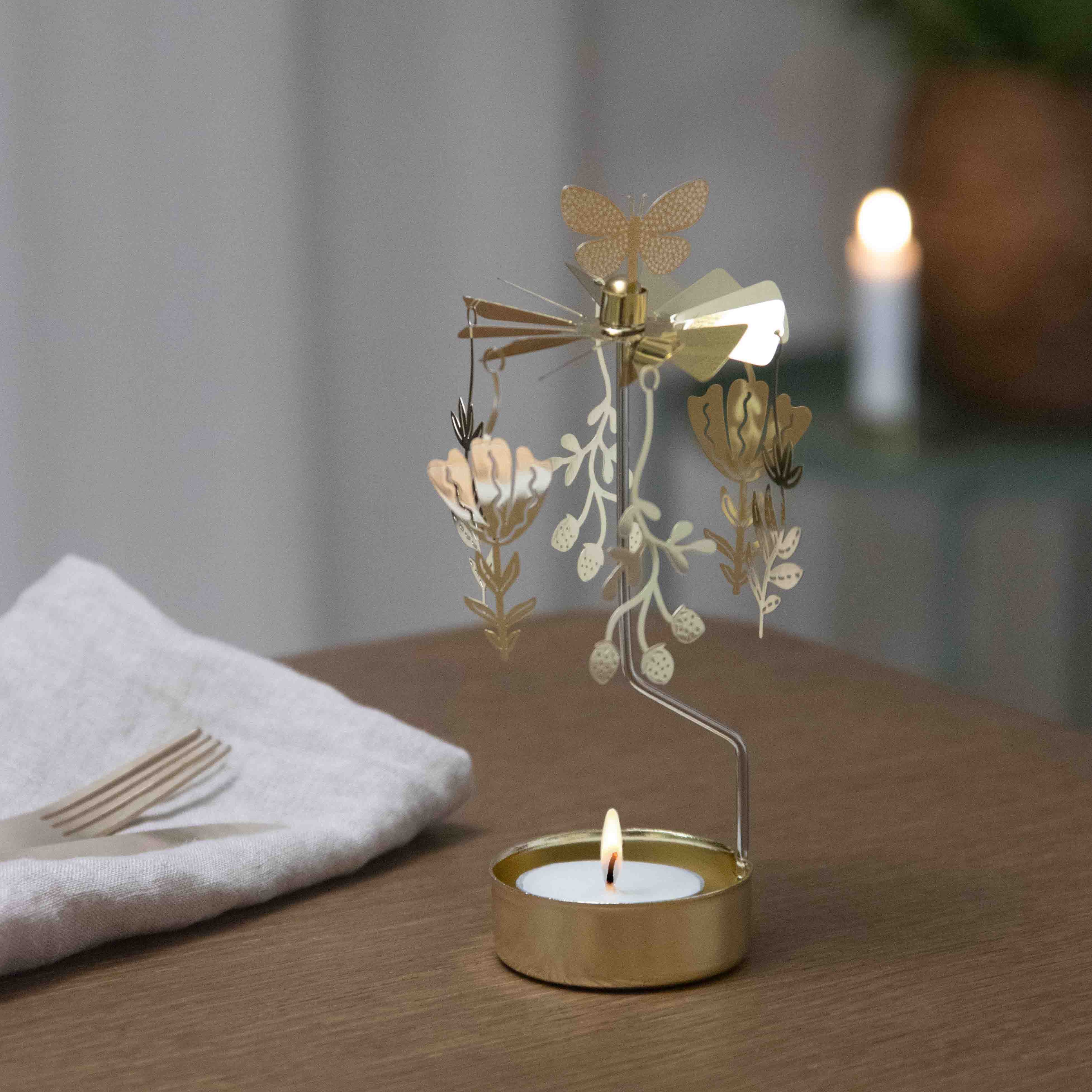 Decorative gold candle holder with a lit candle on a wooden surface.