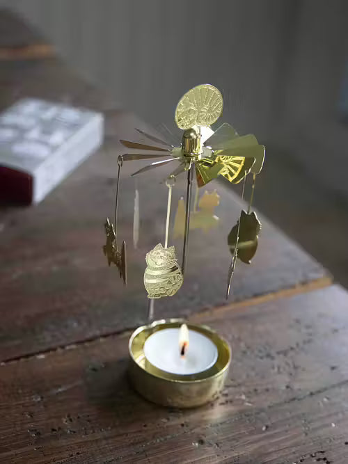 Decorative gold candle windmill with animal shapes on a small candle in a rustic setting