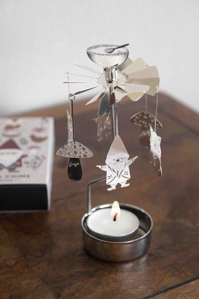 Decorative angel with hanging figures on a candle holder with a lit candle.