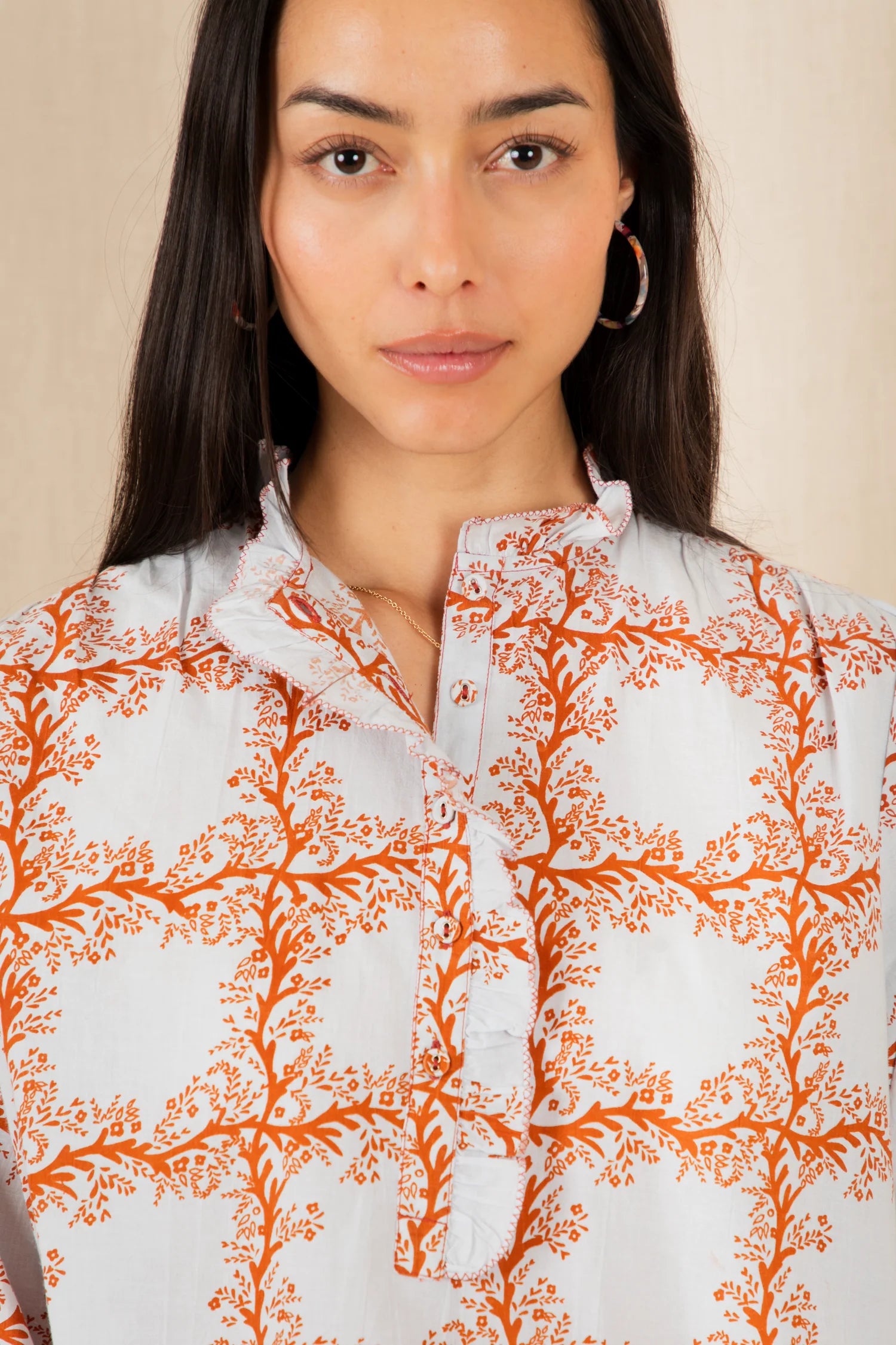 Woman wearing a white shirt with orange floral patterns against a beige background