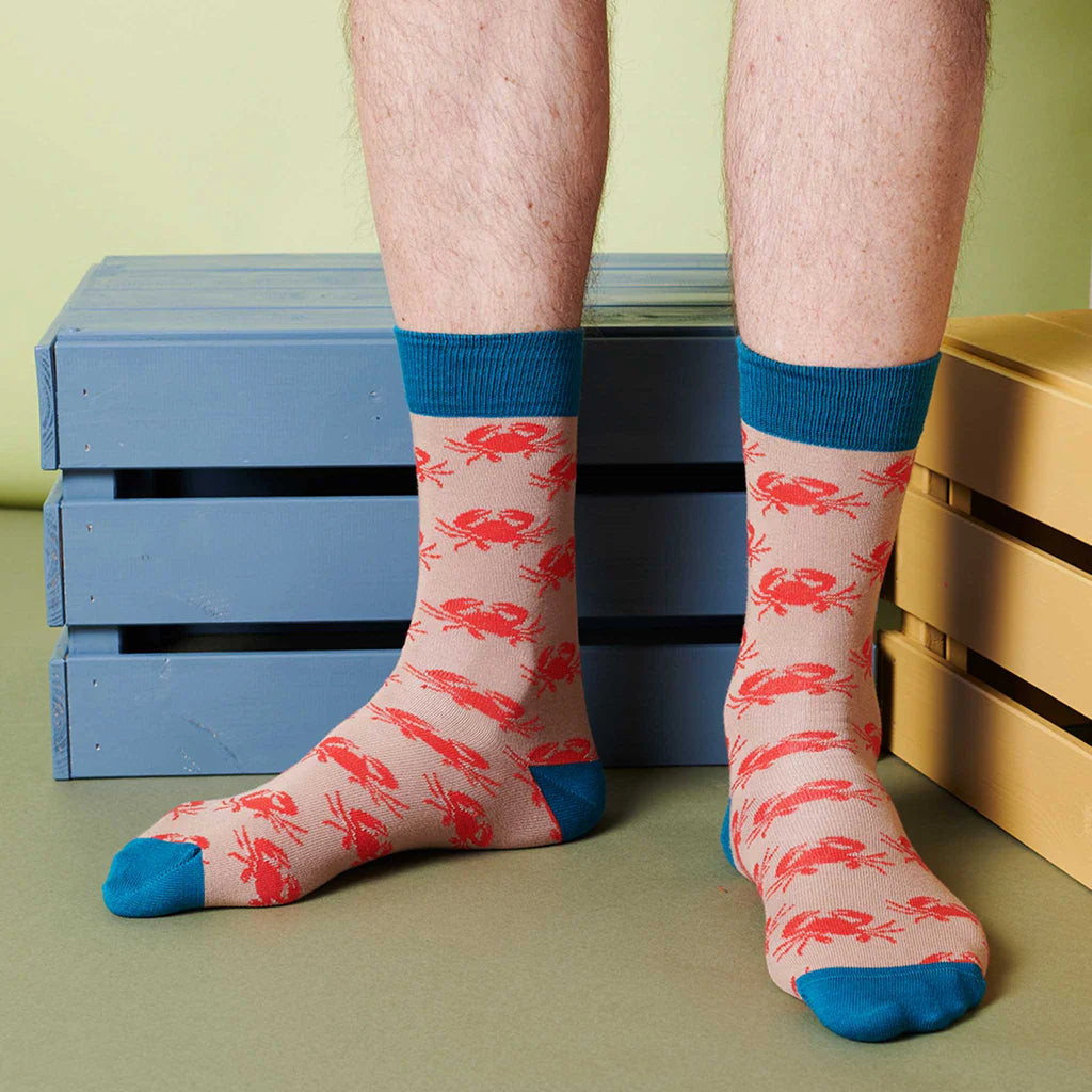 Beige crew socks with a repeating pattern of red crabs and teal cuffs.