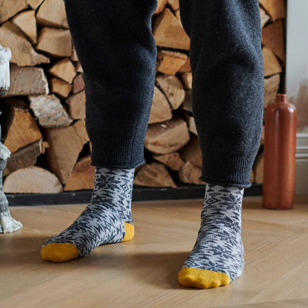Pair of grey wool socks with a dark grey snowflake pattern and mustard yellow cuffs.