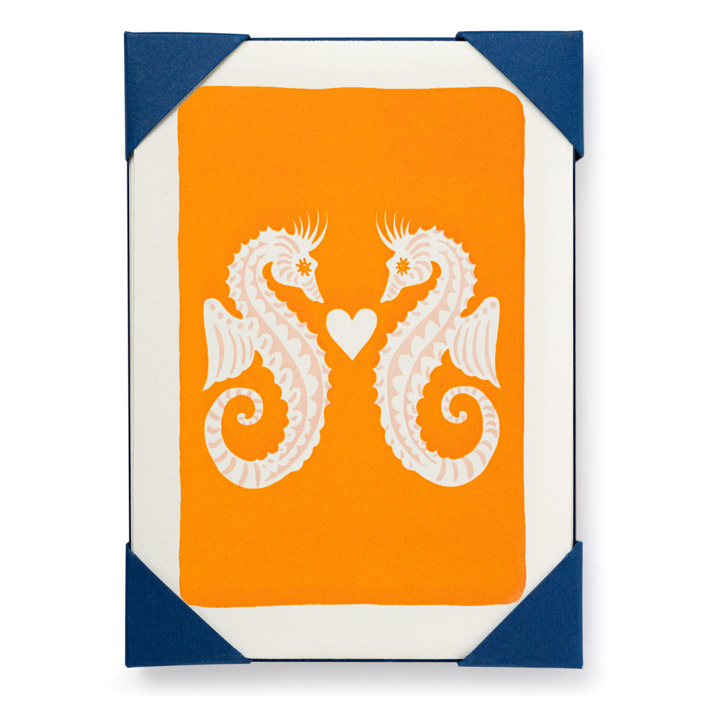 Orange card with two stylized pink seahorses facing each other, a small heart between them.