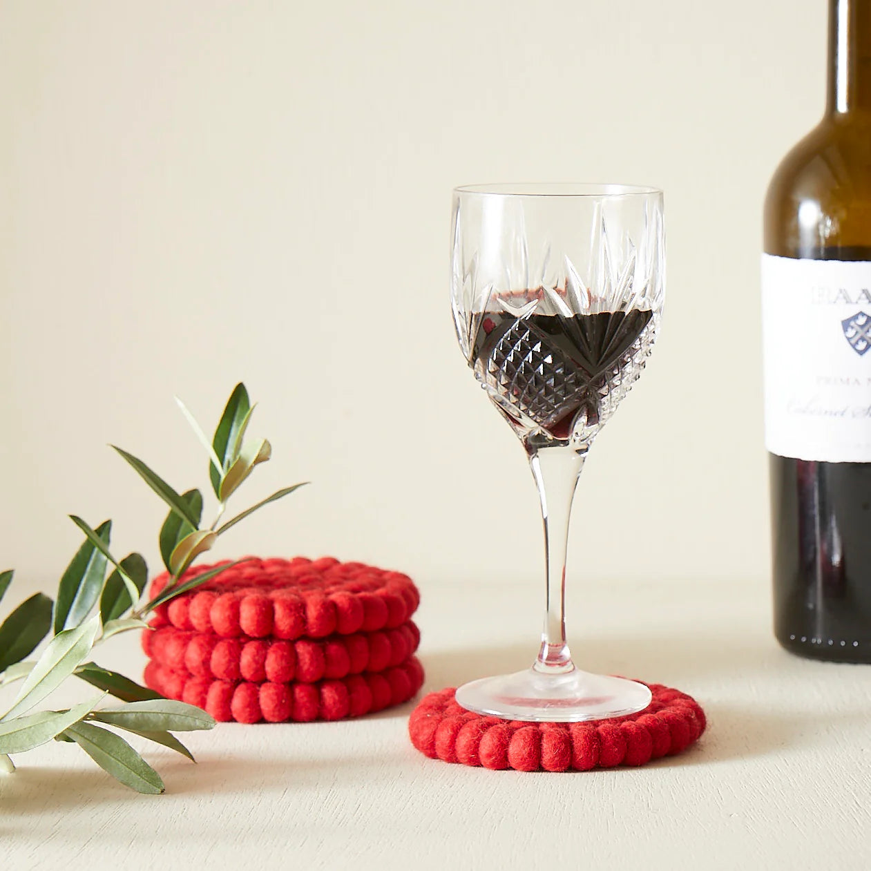 Set of three red felt coasters with a textured surface, one supporting a wine glass.