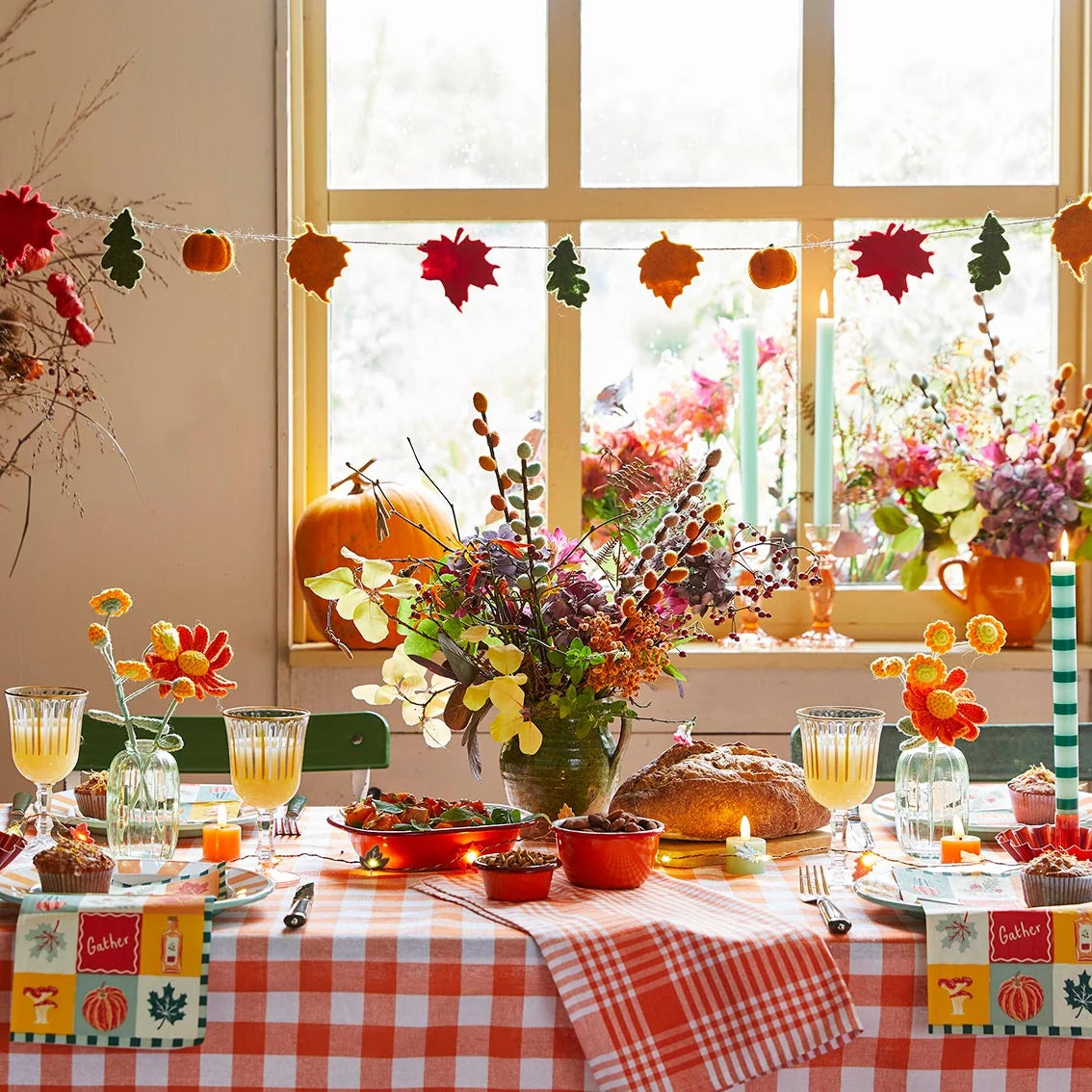 Decorated table with fall-themed centerpieces, pumpkins, and a window view of flowers.