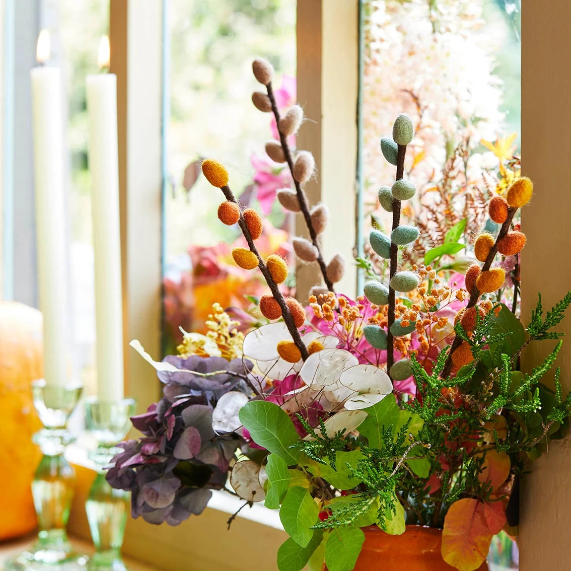 Decorative floral arrangement with pumpkins and candles in front of a window.