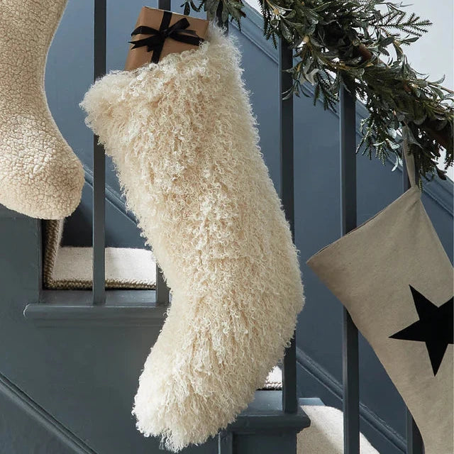Chalk UK fluffy cream stocking hanging on a staircase, adorned with a gift tied with a black ribbon.