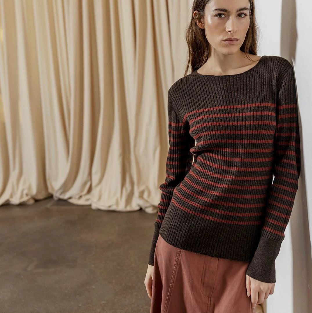 Woman wearing a black and red striped sweater against a beige curtain background
