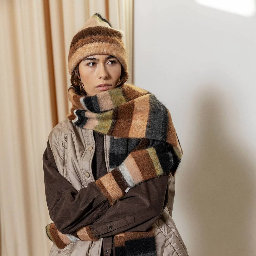 Person wearing a striped scarf and hat in a neutral setting