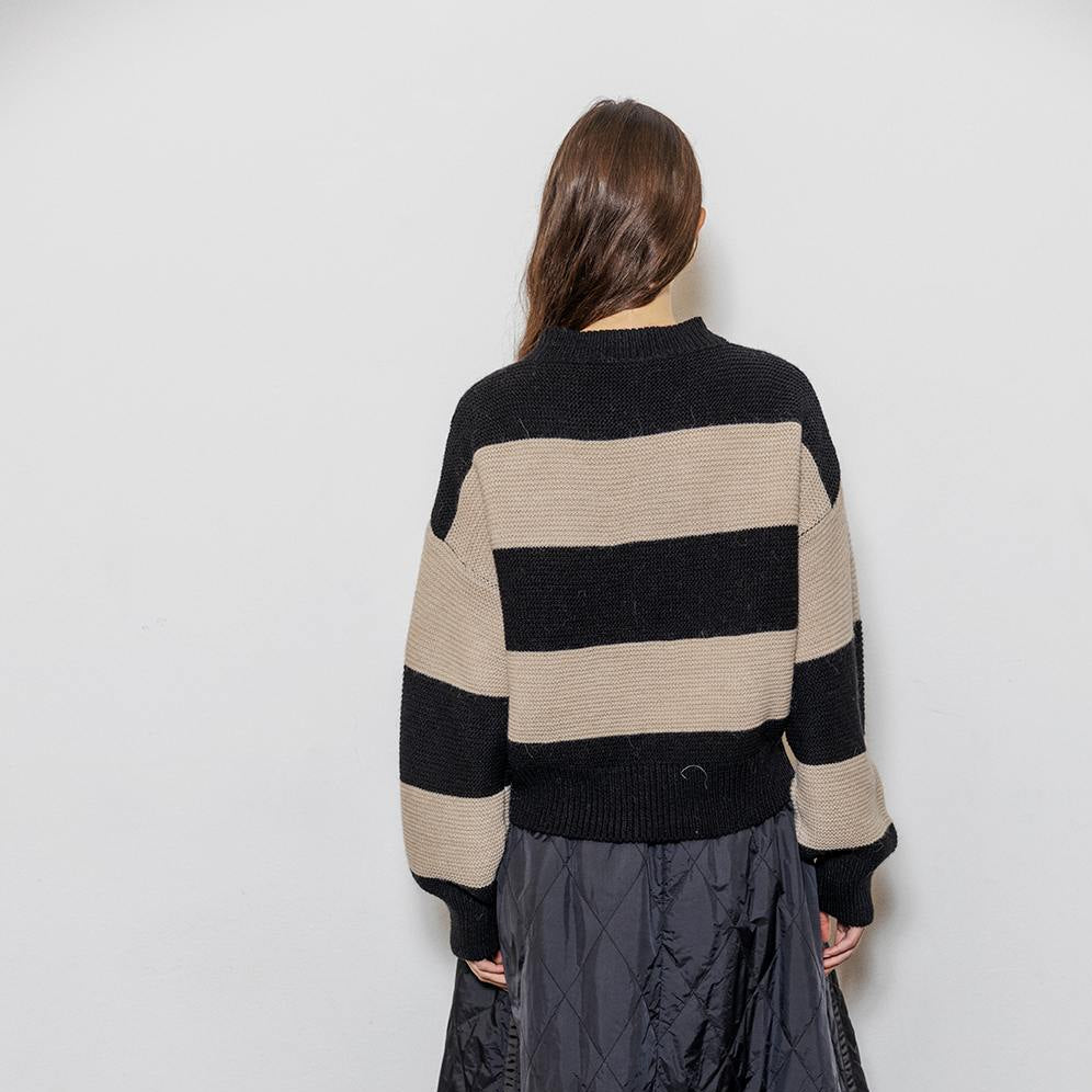 Person wearing a striped sweater and long dark skirt against a white wall.