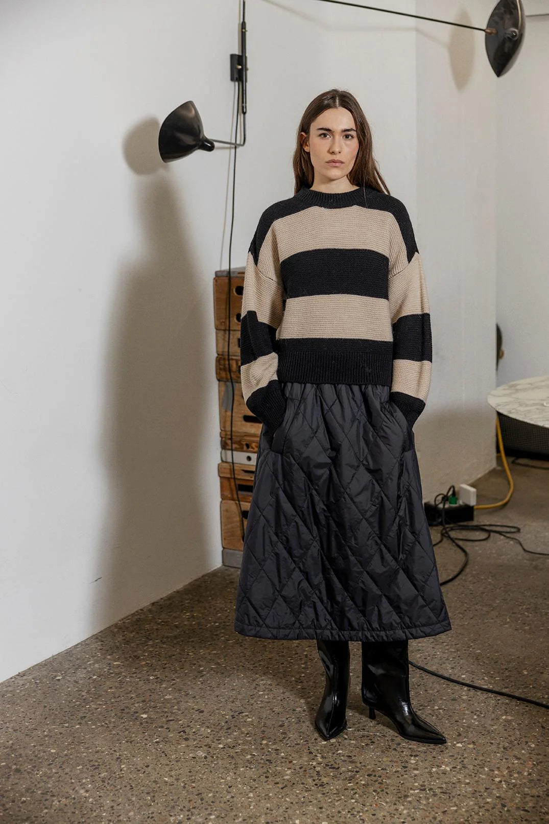 Woman wearing a striped sweater and black quilted skirt in an indoor setting.