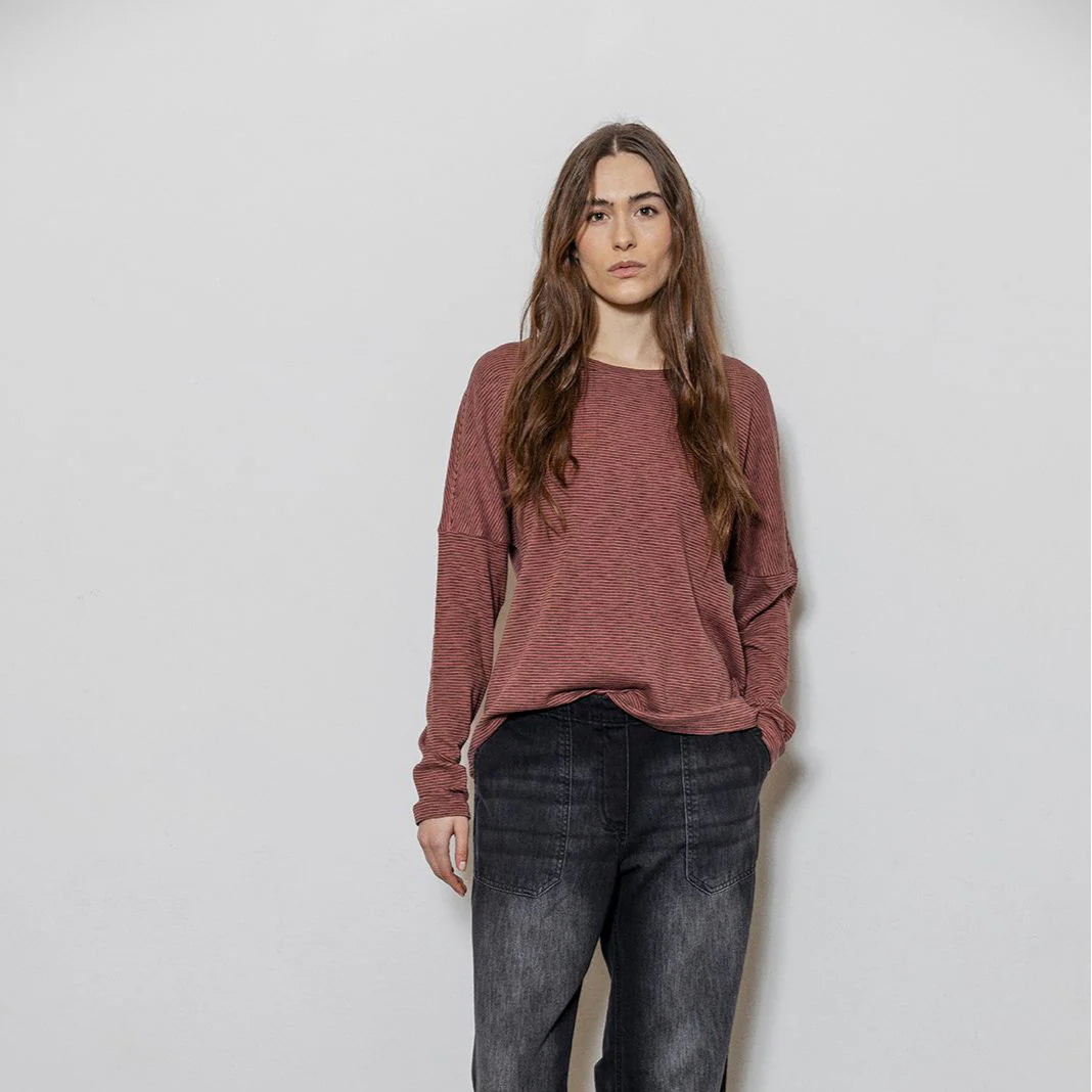 Woman wearing a red sweater and black jeans against a white wall.