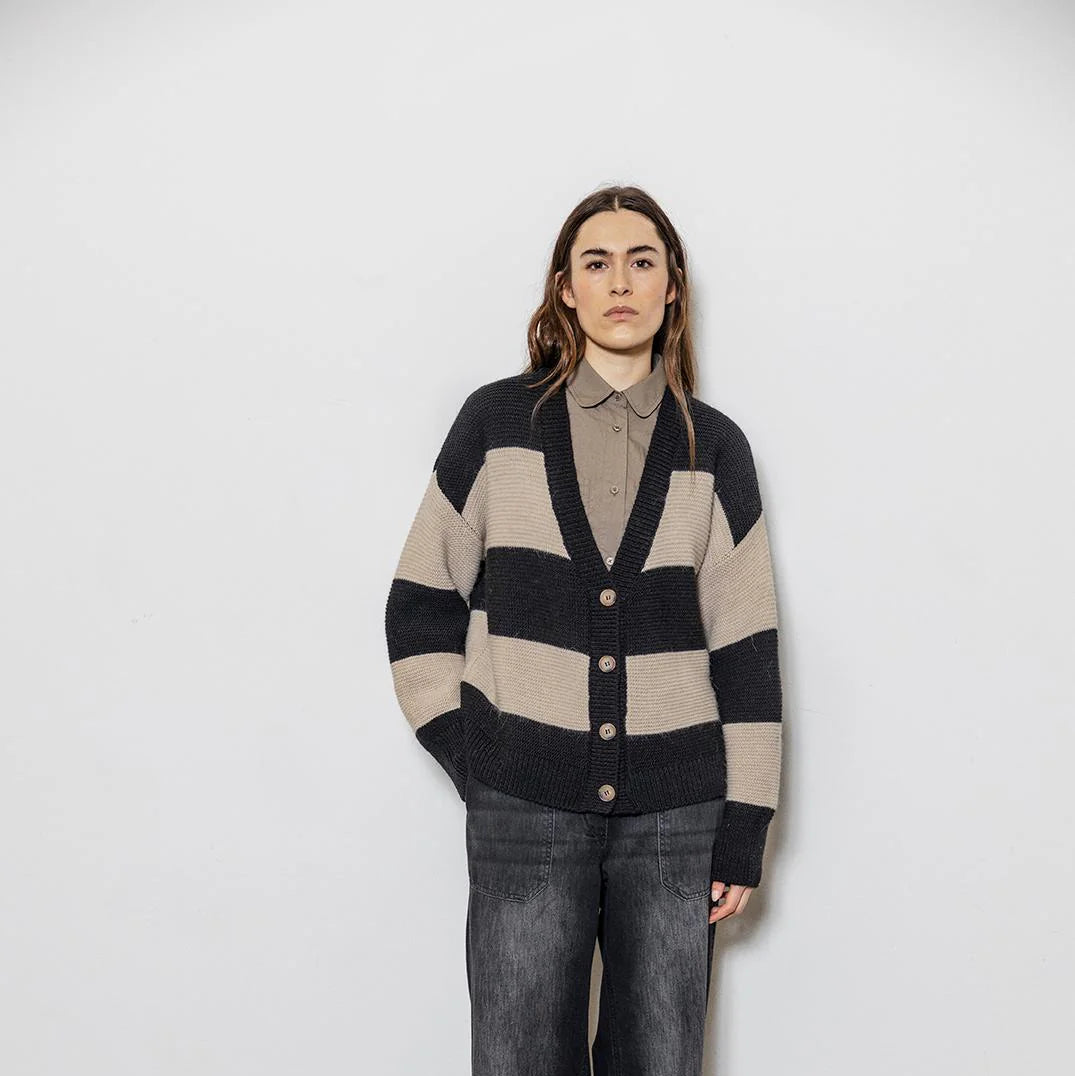 Person wearing a striped sweater and jeans against a white wall