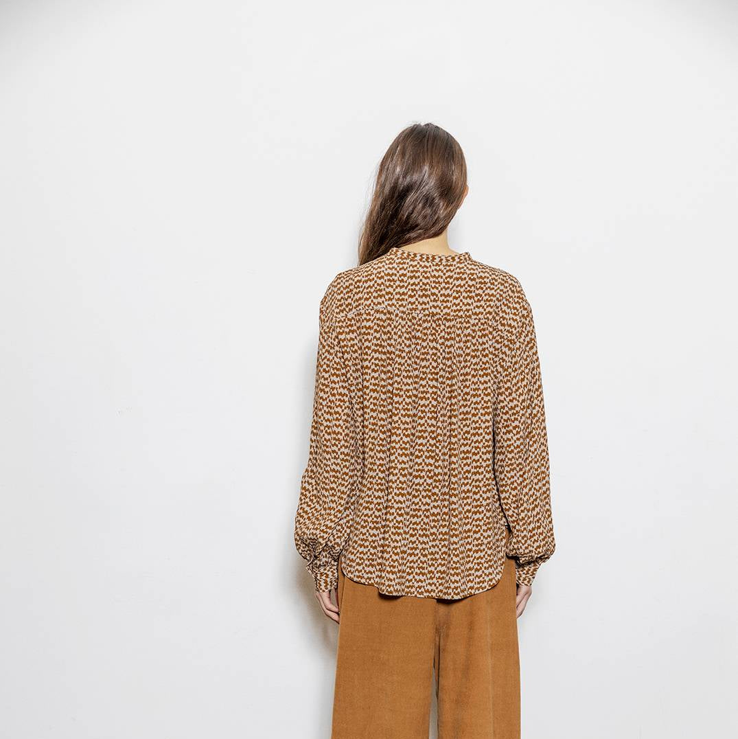 Person wearing a patterned sweater and brown pants against a white wall.