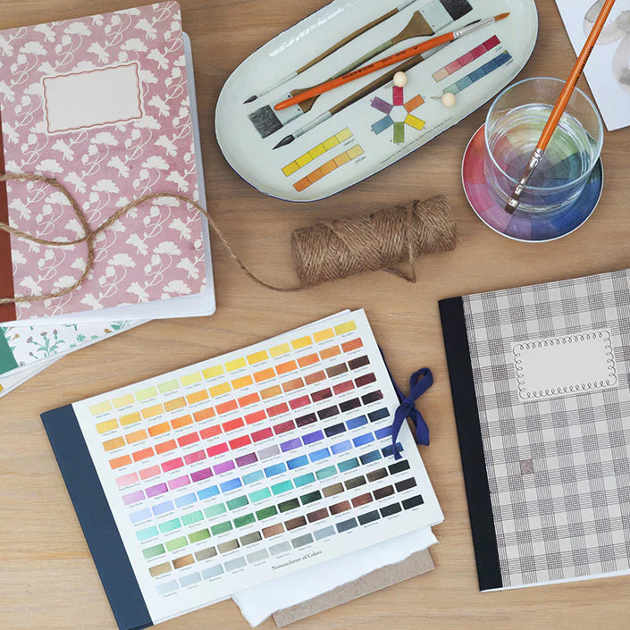 Art supplies including a color swatch, paintbrushes, and a notebook on a wooden surface.