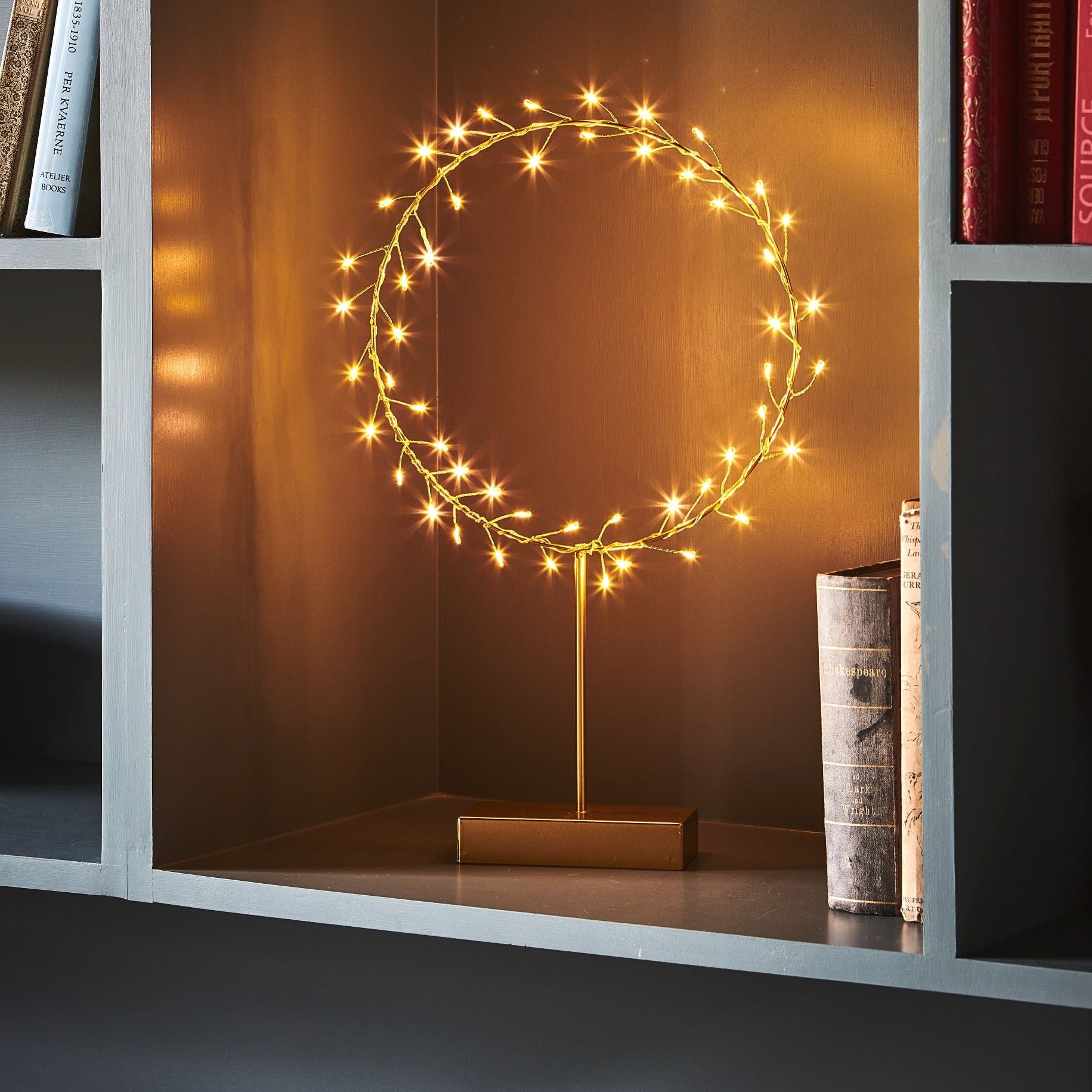 Gold circular LED light fixture with warm-toned lights, on a gold stand.