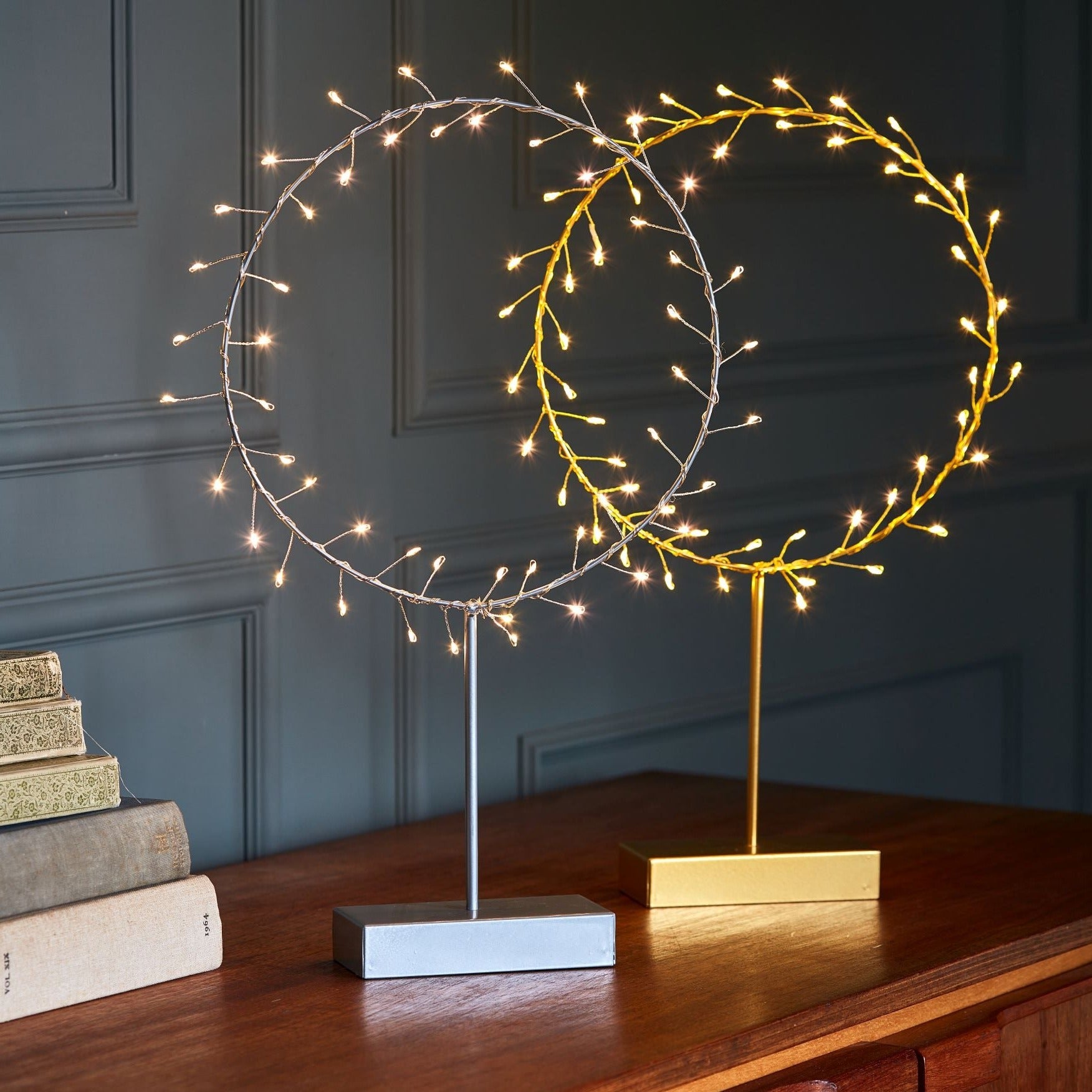 Two circular LED light displays on stands; one silver, one gold.  Each features warm-white lights along a wire frame.