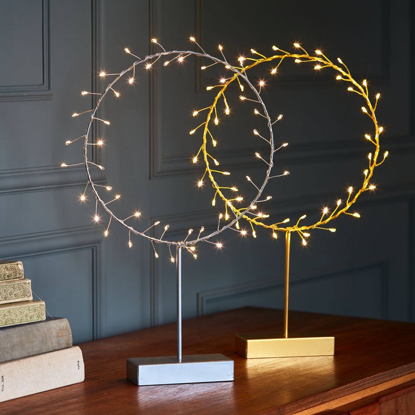 Two illuminated circular wire light displays on stands. One is silver, the other gold.