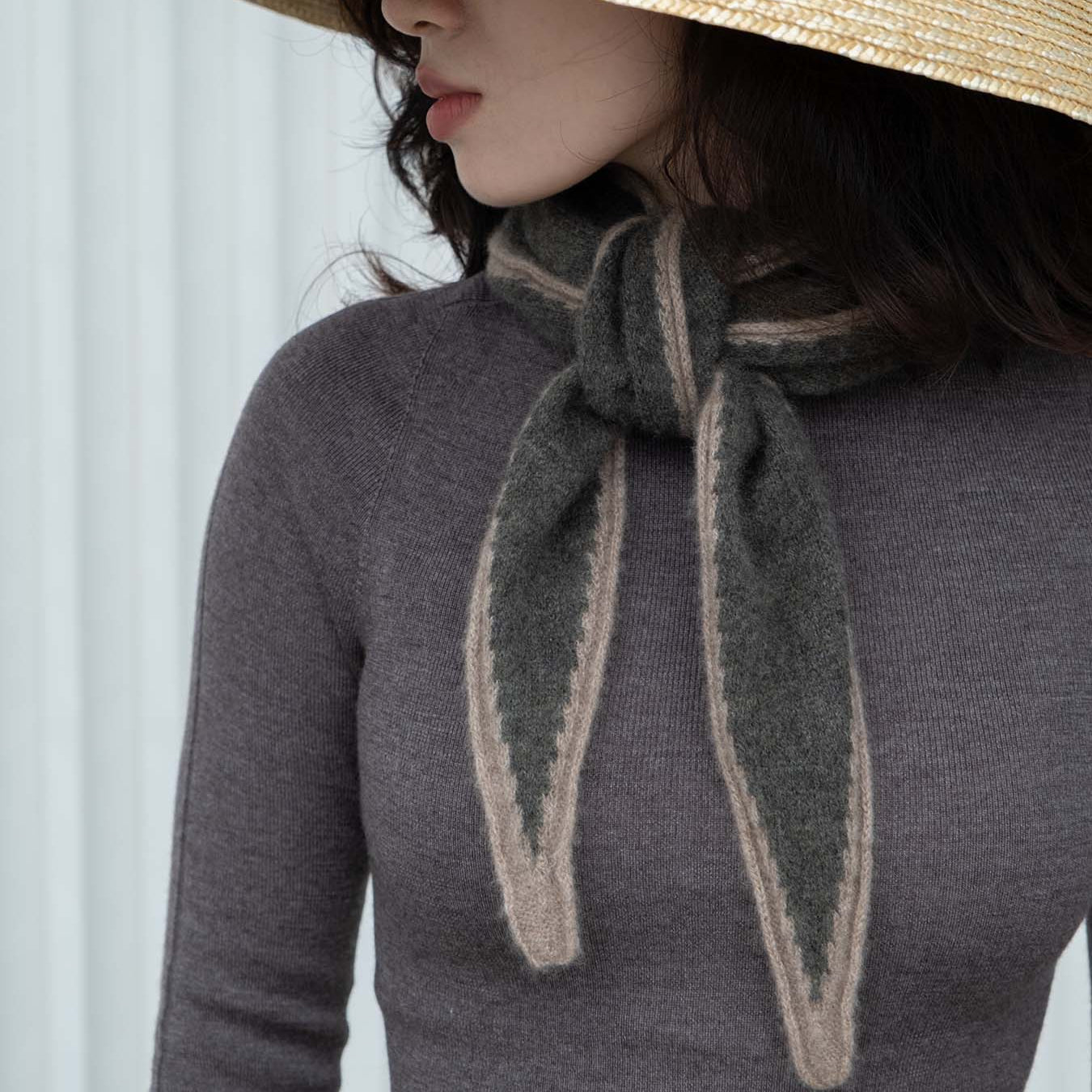 Person wearing a dark gray sweater with a matching scarf, standing against a white background.