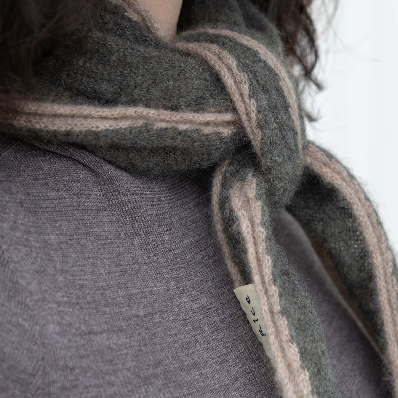 Close-up of a person wearing a dark gray scarf with beige stripes, focusing on the scarf and part of the person's clothing.