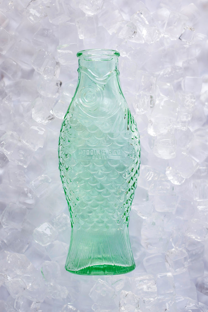 green, pressed glass carafe, set against ice cubes, from the Fish & Fish tableware collection, by Italian designer Paola Navone, for Belgian design brand Serax.