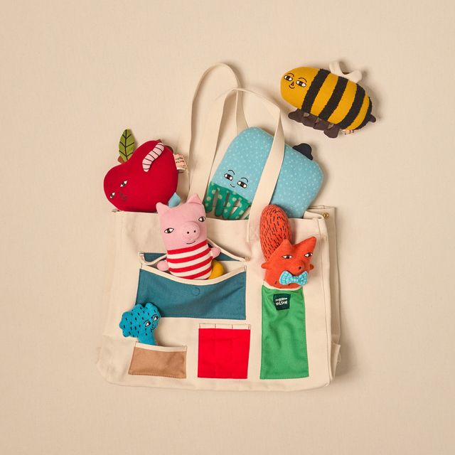 Colorful soft toys shaped like animals and a bee on a beige tote bag against a beige background