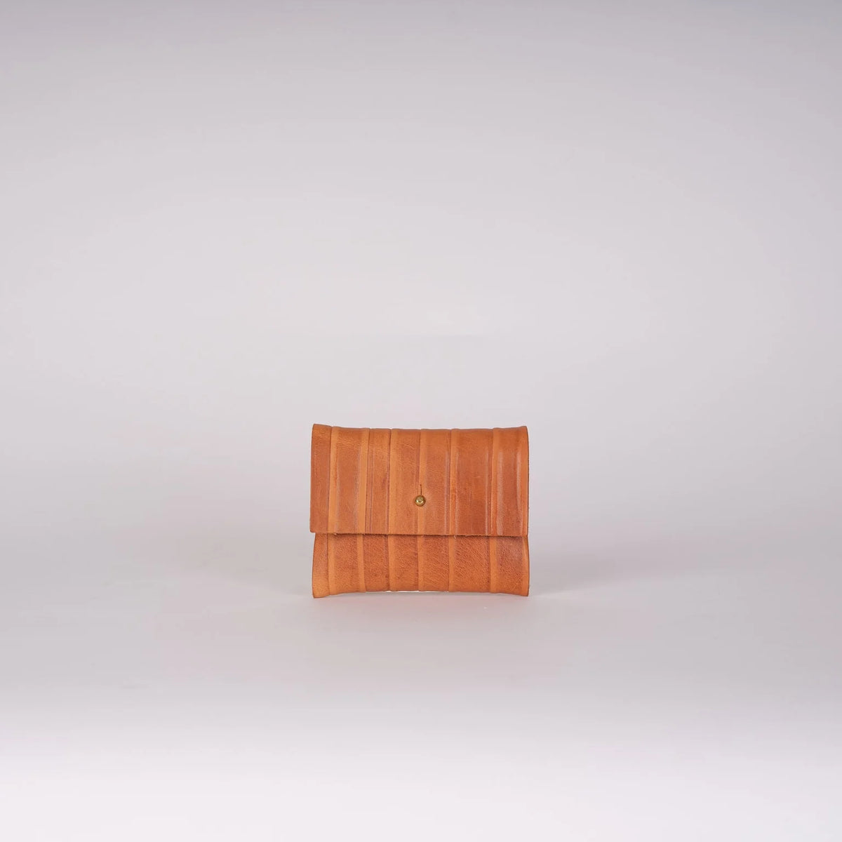 A small tan leather clutch or wallet with a vertical pleated texture and a small gold button closure, centered on a light gray background.