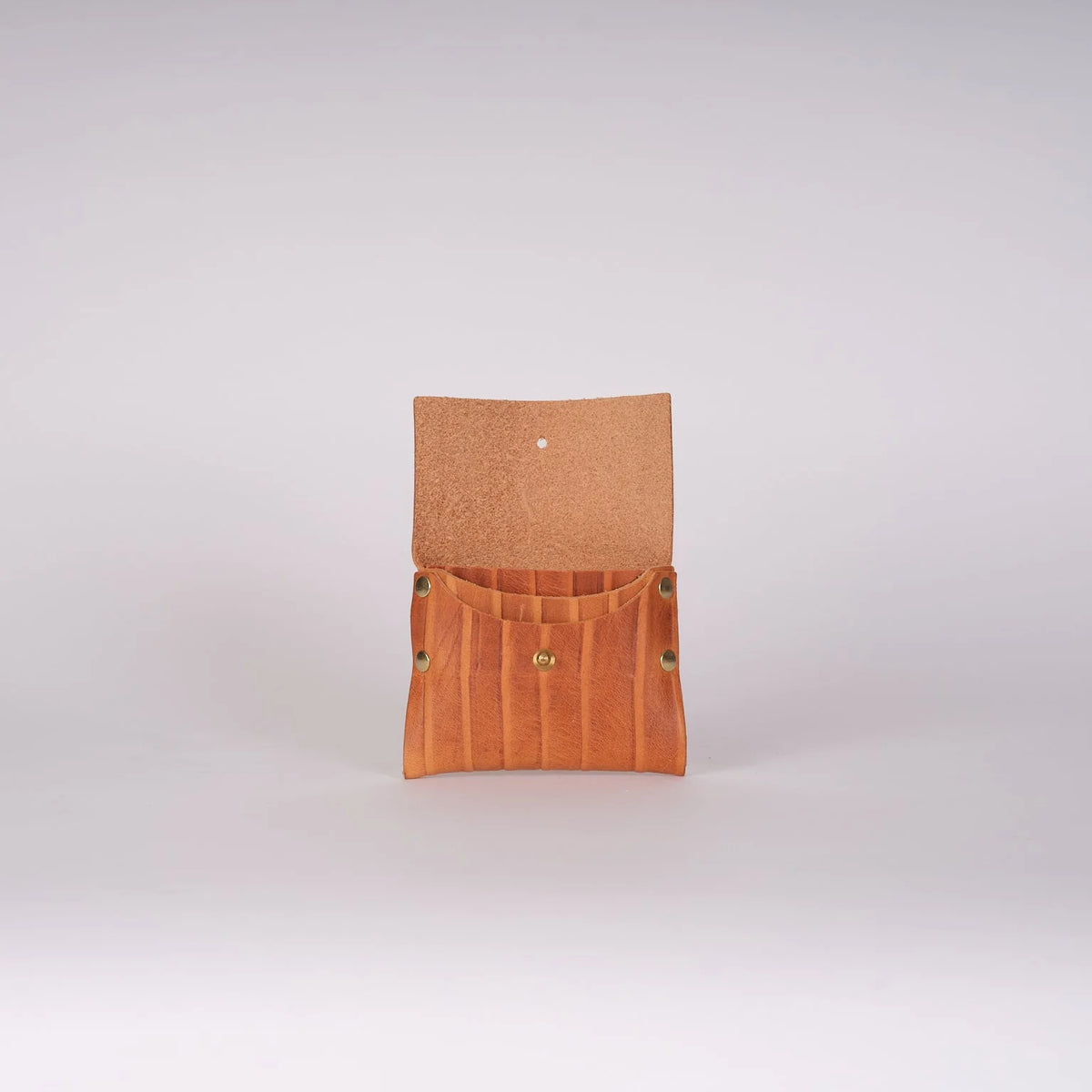 A small tan leather pouch or organizer with a fold-over flap and vertical stitched compartments, shown open against a plain light gray studio background.