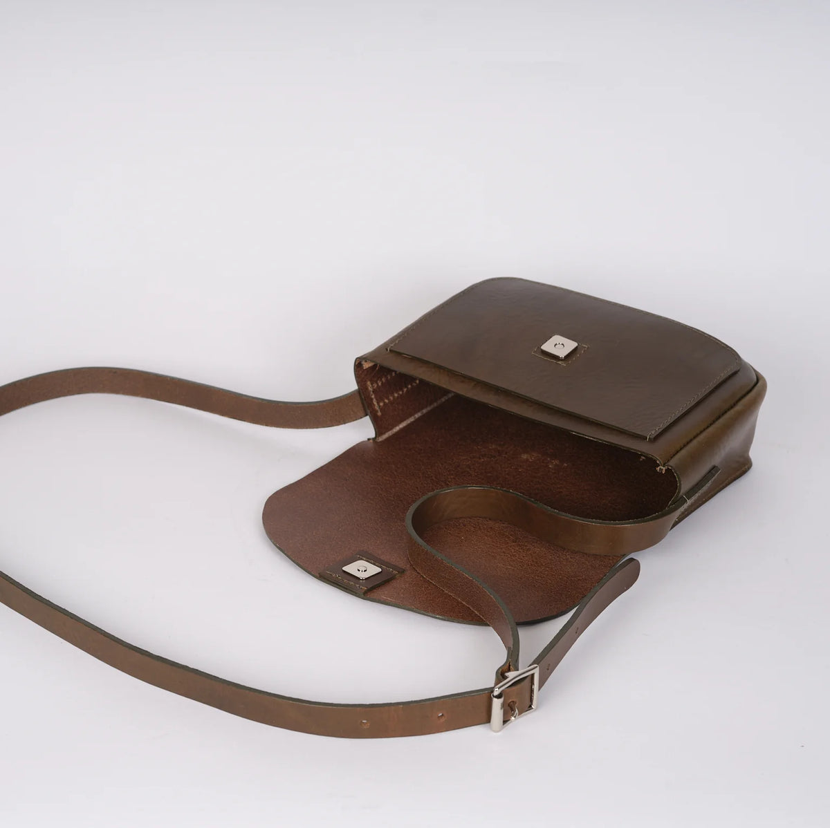 A dark brown leather crossbody bag with a matching adjustable shoulder strap, shown from an angled side view on a light gray background.