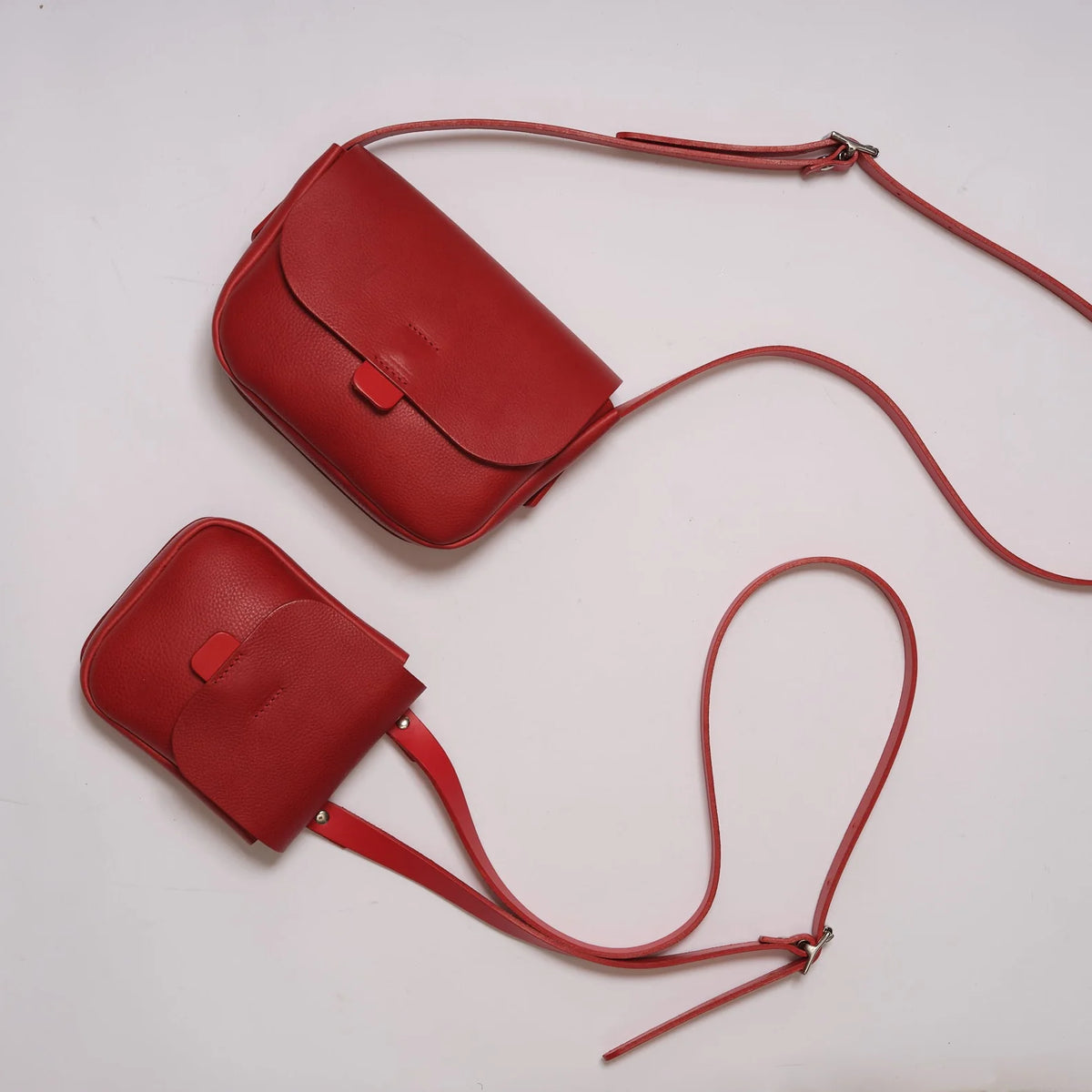 Two red leather crossbody bags of different sizes with matching straps, arranged diagonally on a plain white background.