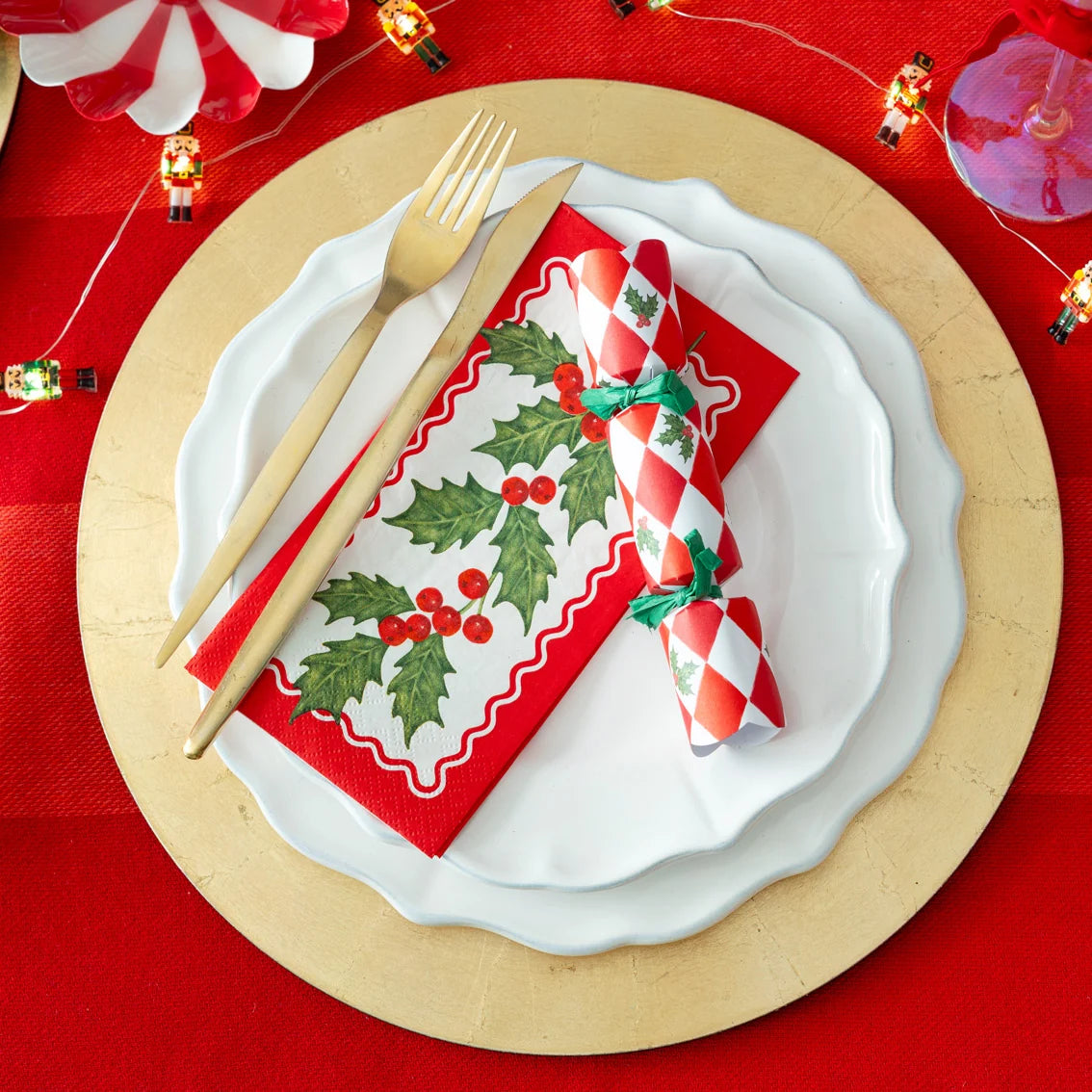 Christmas-themed place setting with holly design on a red tablecloth.