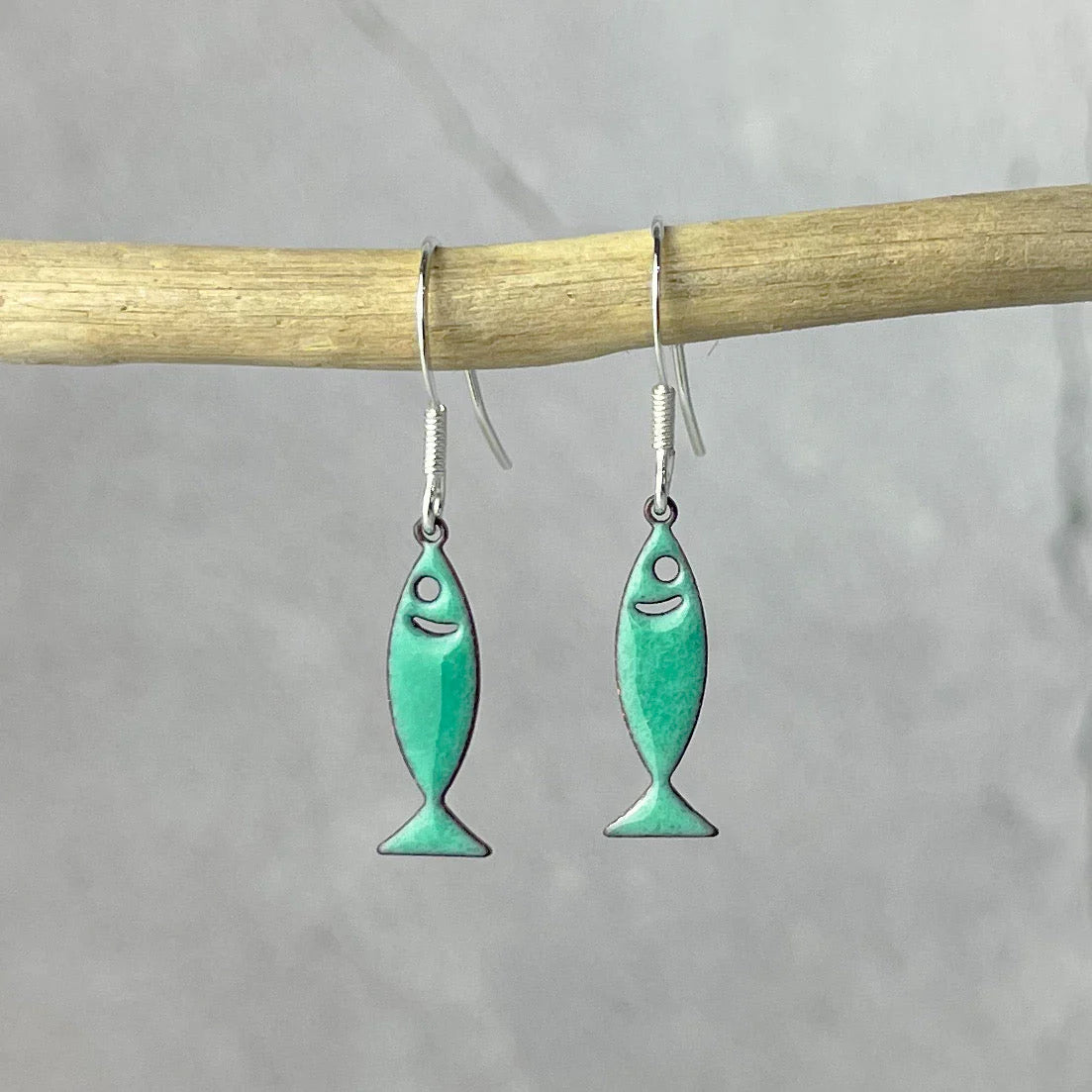Turquoise fish-shaped earrings hanging on a stick against a gray background
