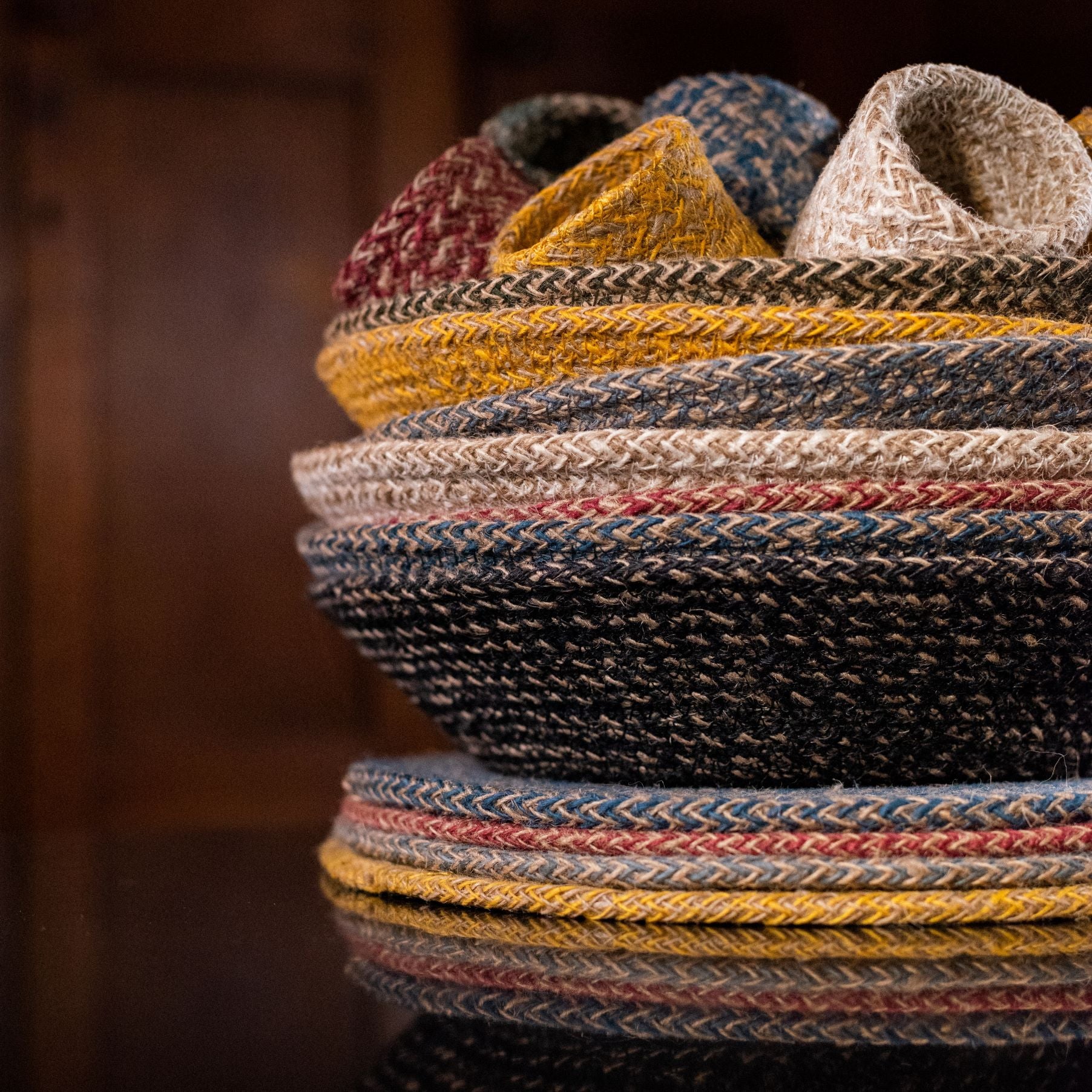 Stack of woven jute coasters in various colors, including natural, mustard yellow, dark blue, and burgundy.