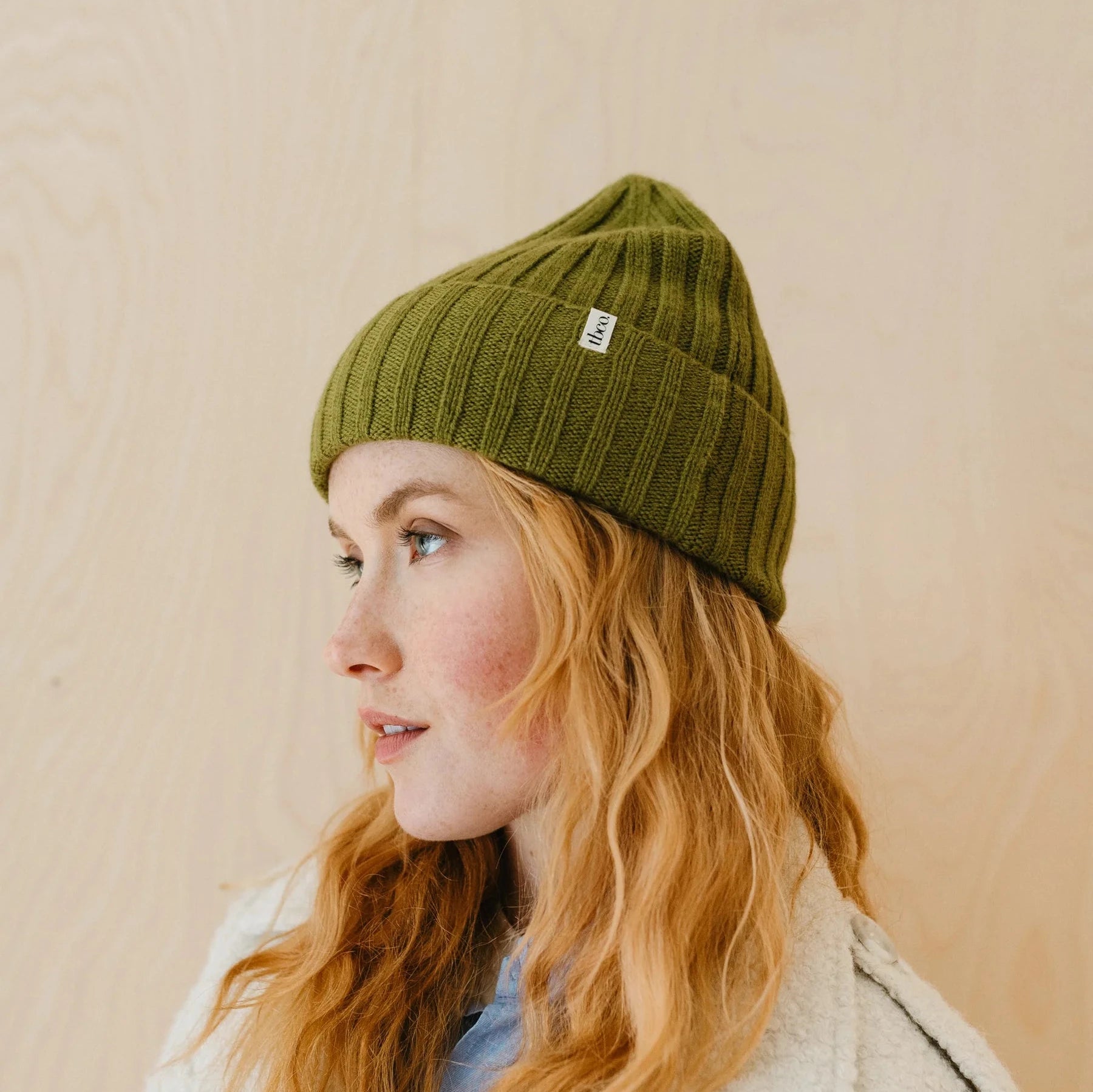 Olive green ribbed knit beanie with a small label.