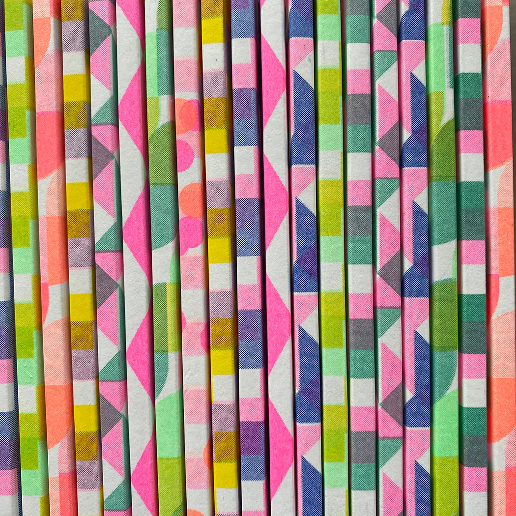 Stack of notebooks with vibrant geometric patterns in pink, green, yellow, and blue.