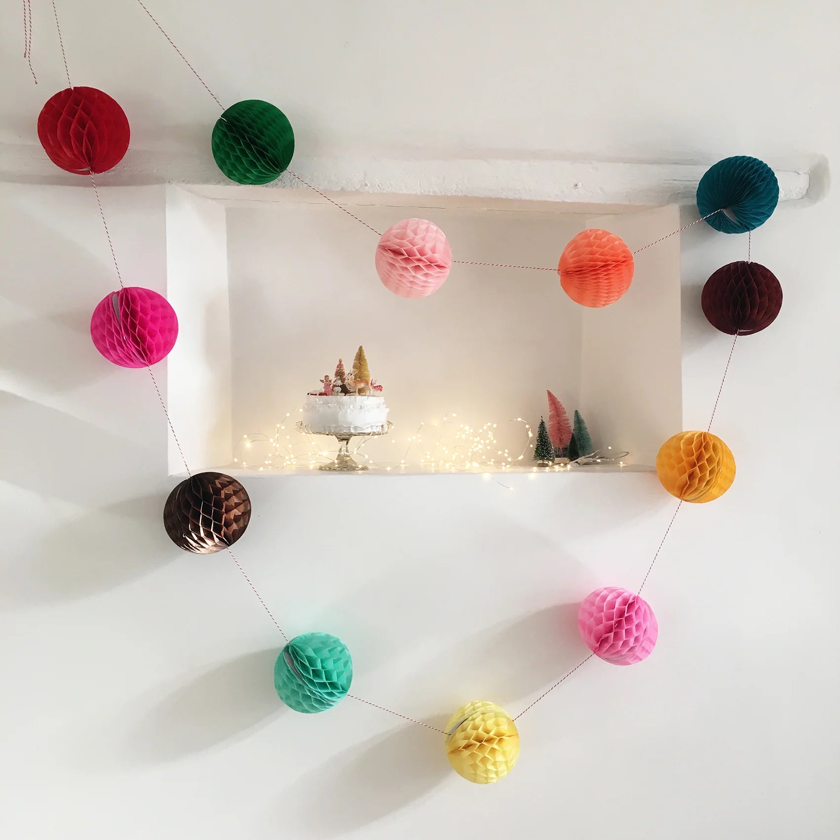 Garland of colorful honeycomb paper balls strung on thin red and white twine.