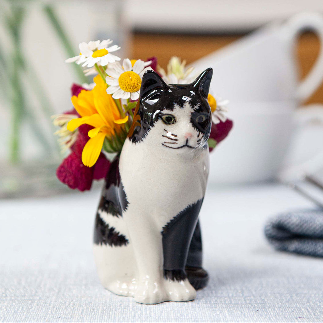 Cat figurine holding a bouquet of flowers on a table with a blurred background