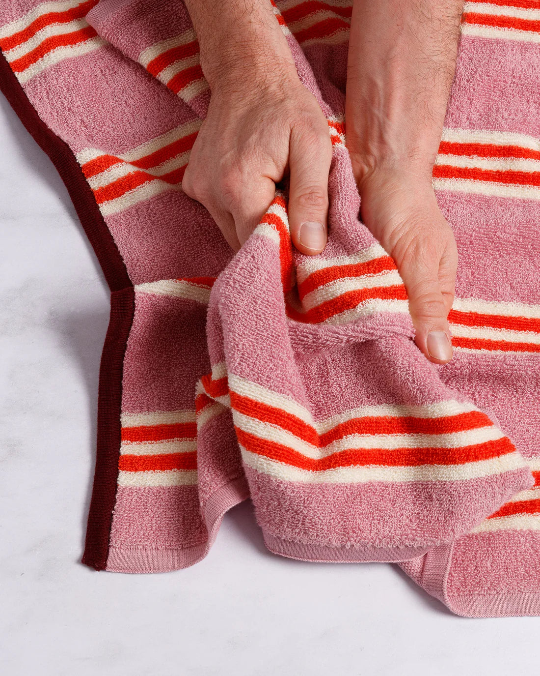 Person holding a pink towel with red and white stripes on a white background
