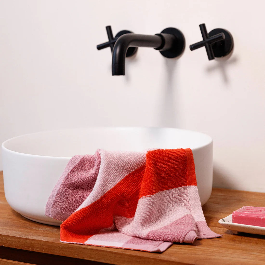 White sink with a red and pink striped towel draped over it, black faucet, and soap on a wooden surface.