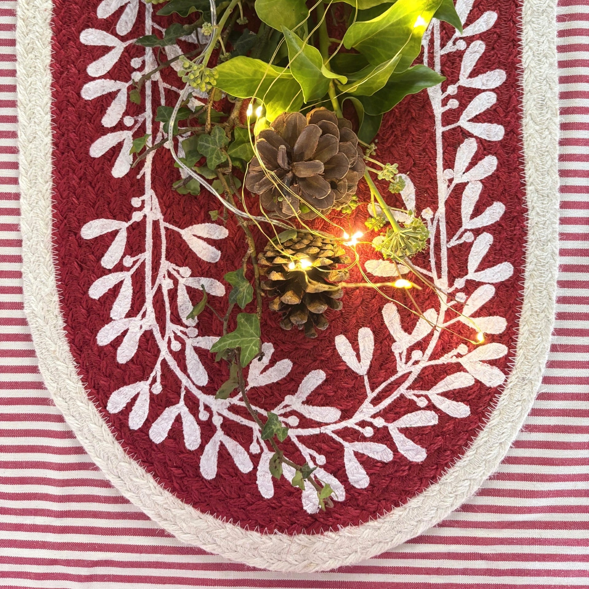 Decorative wreath with greenery, pine cones, and string lights on a red and white striped background.