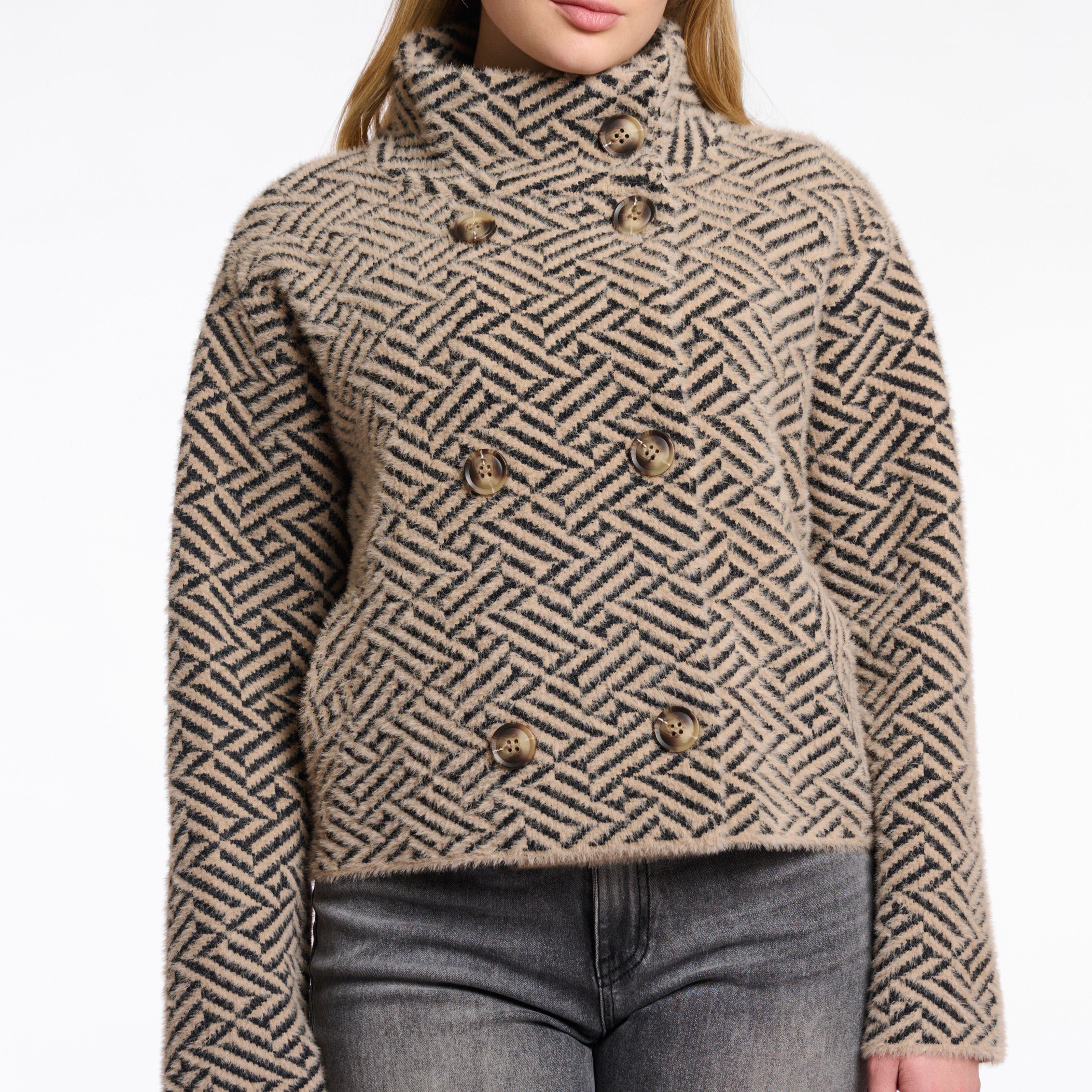 A woman wearing a short double-breasted jacket with a geometric sand graphic pattern, featuring a stand-up collar and large buttons.