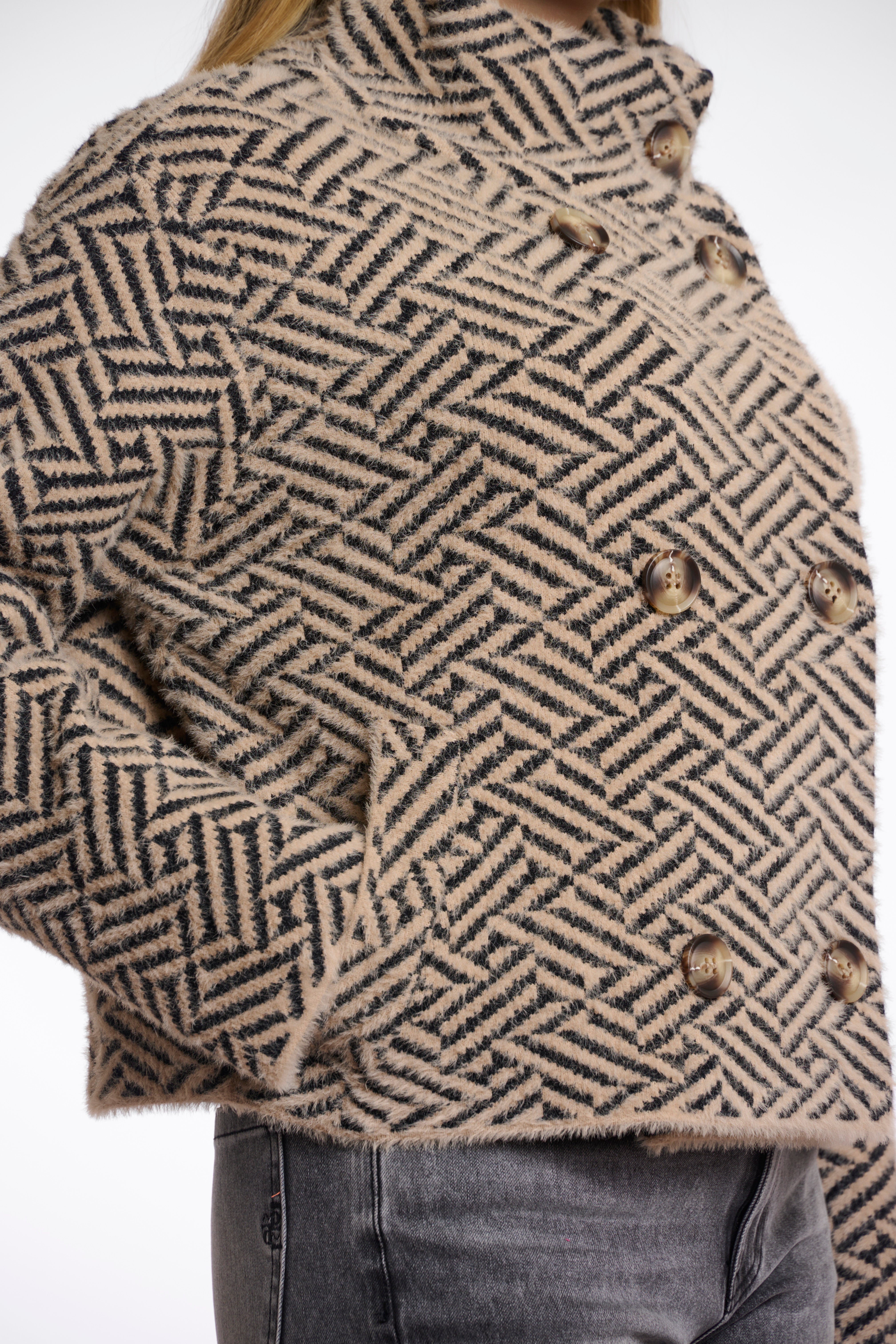 A woman wearing a short double-breasted jacket with a geometric sand graphic pattern, featuring a stand-up collar and large buttons.
