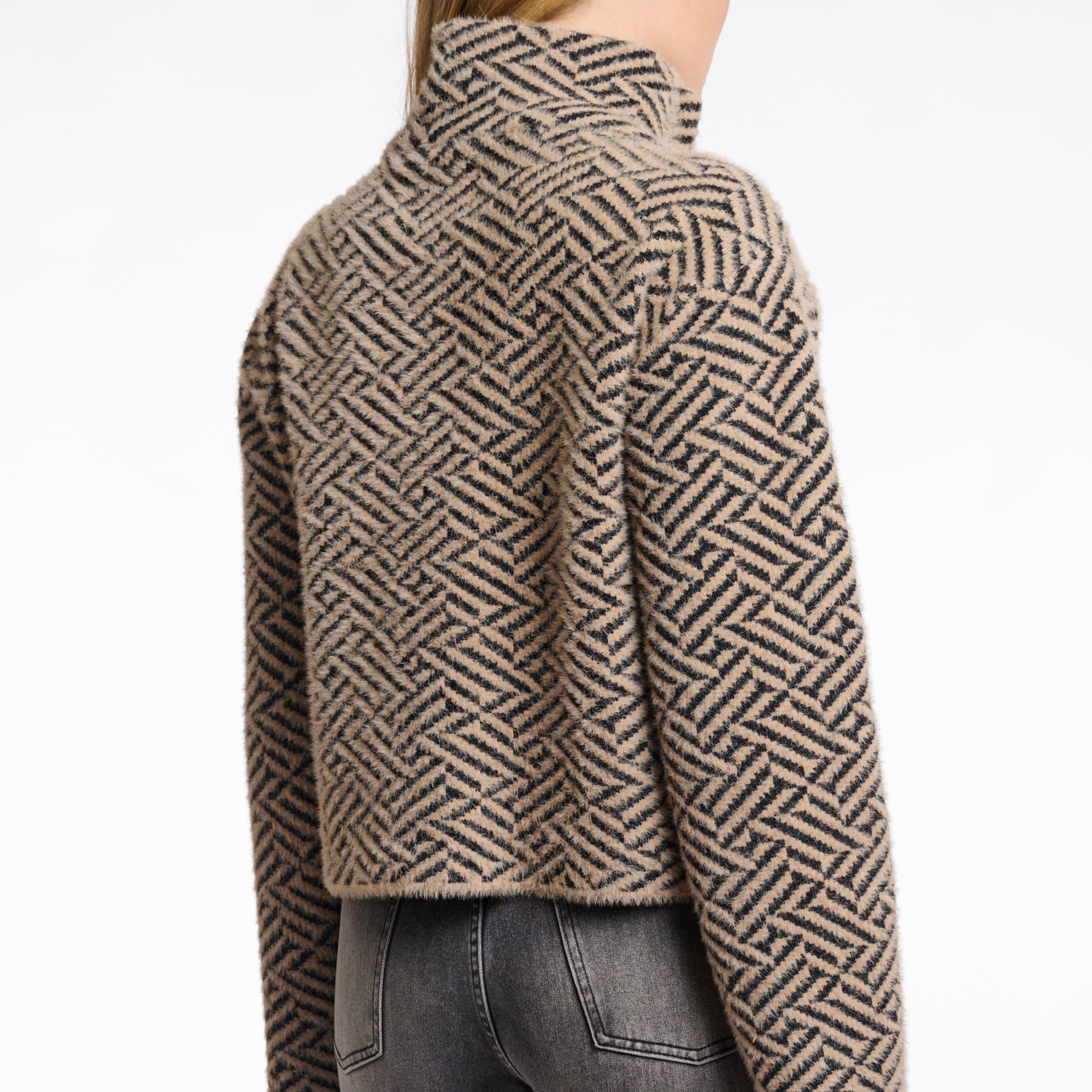 A woman wearing a short double-breasted jacket with a geometric sand graphic pattern, featuring a stand-up collar and large buttons.