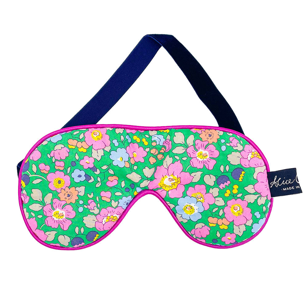 Floral sleep mask with green background, pink and other colored flowers, dark blue headband, and hot pink trim.