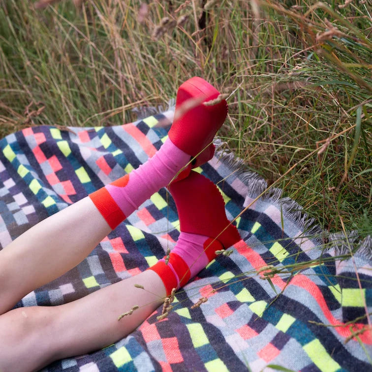Pink and red socks by Donna Wilson on a patterned blanket in a grassy field.