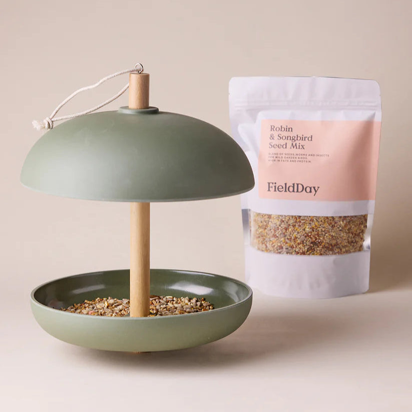 Green bird feeder with a bag of FieldDay bird seed on a beige background