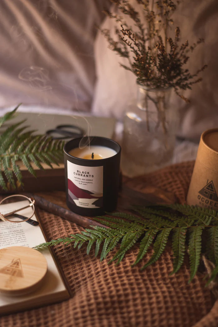 Black Currants natural soy candle in a black jar with a minimalist label.  A wisp of smoke rises from the lit candle.