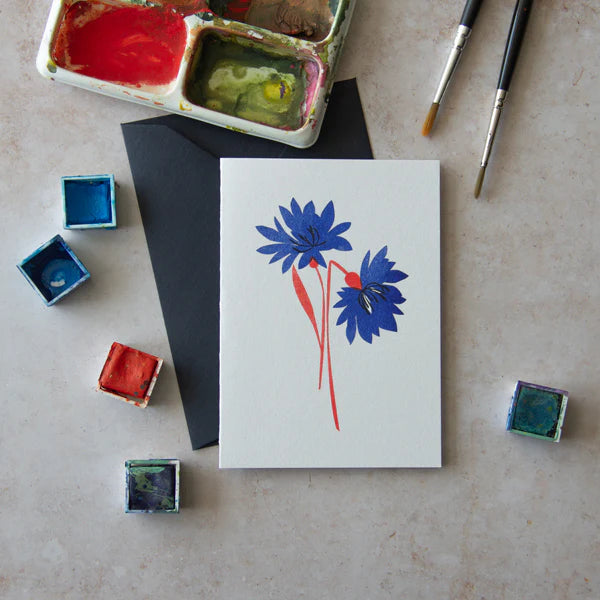 Greeting card featuring a stylized illustration of two blue cornflowers with red stems.