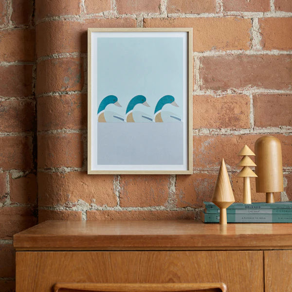Framed print of three stylized mallard ducks in teal and beige, arranged in a row.