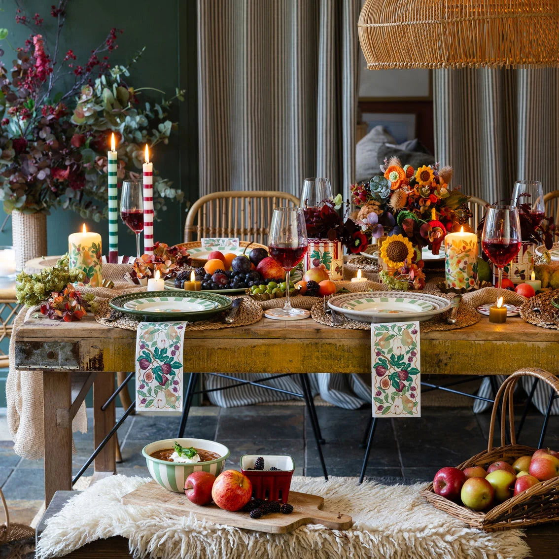 Decorative table setting with candles, fruit, and flowers in a cozy room.